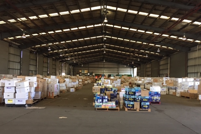 A large warehouse with pallets of stationary scattered throughout.
