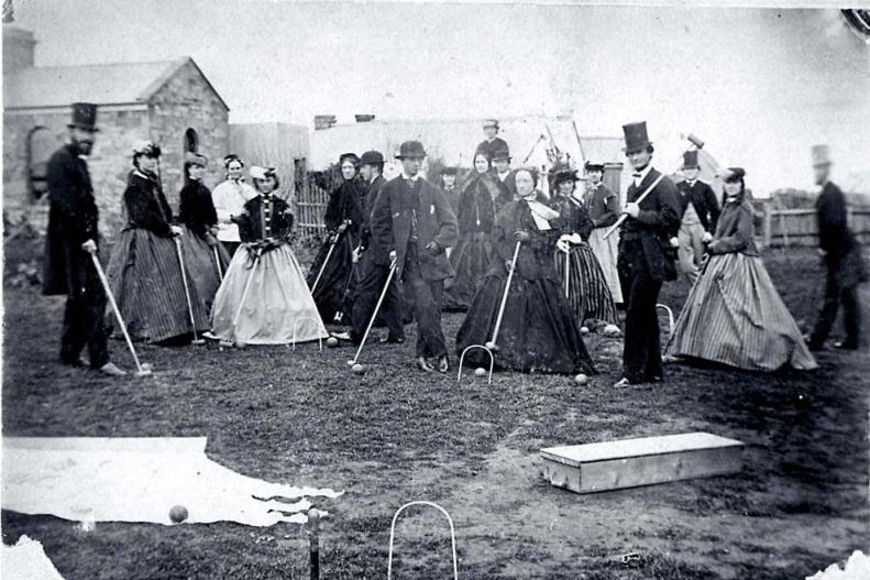 Black and white image of people posing for a photo with croquet hammers in 1868.