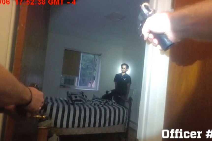 A man is seen from a police body camera standing in a room with police guns pointed at him.