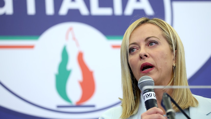 Italy's new PM Giorgia Meloni holding microphone on the right, brothers of italy logo in background