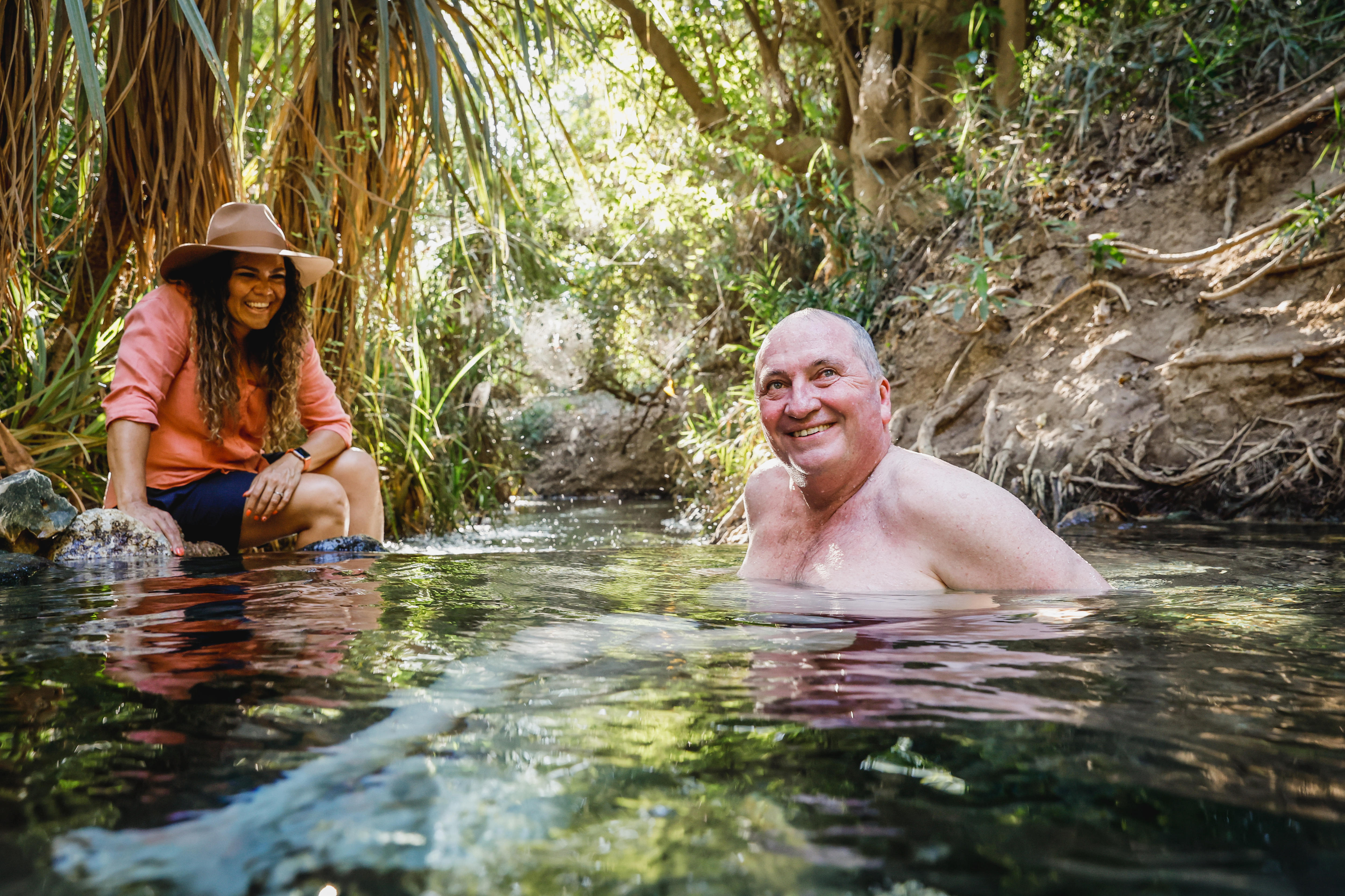 A man sits in a freshwater spring while a clothed woman appears to be amused