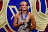 Emily Bates smiles in front of the AFLW Best and Fairest signage with a glass of champagne and her medal