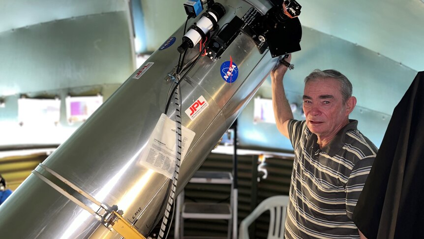 A man wearing a polo shirt standing in a dome shaped room with a hand on a large metal telescope