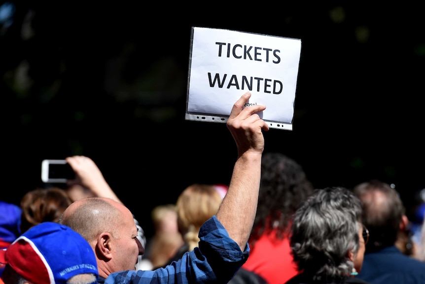 A fan holds up a piece of paper that says "tickets wanted" at the 2016 AFL grand final parade in Melbourne.