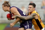 A Fremantle Dockers AFL player holds the ball as he is tackled by a Hawthorn opponent.