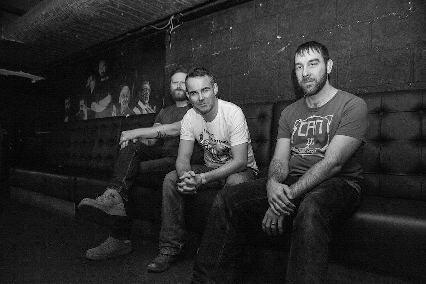 A band sit on a bench in a venue.