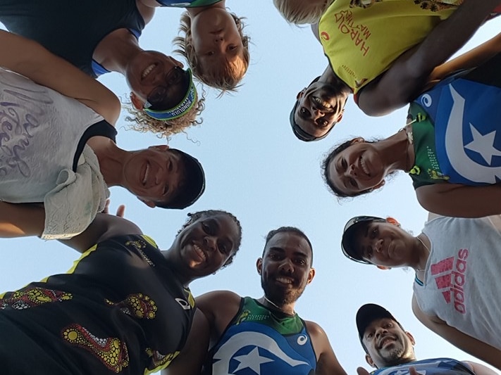 Members of the TI Deadly Runners stand in a huddle looking down at the camera.