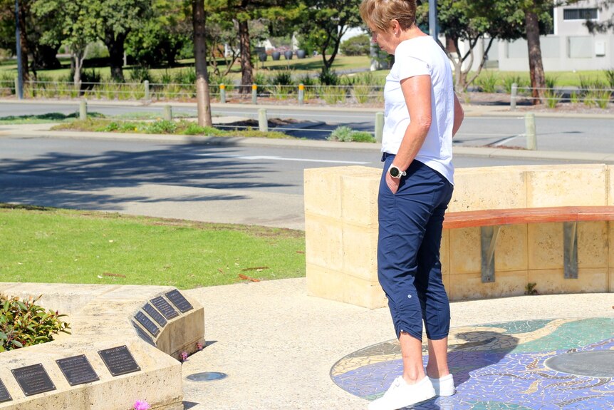 A woman in a white T-shirt and blue trousers looks at names on a memorial.