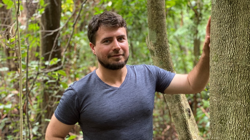 Man standing beside tree trunk in a rainforest.