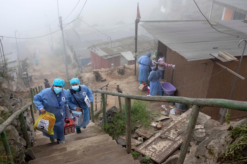 Health workers carry coolers of the Pfizer COVID-19 vaccine up woodern stairs in a remote area.