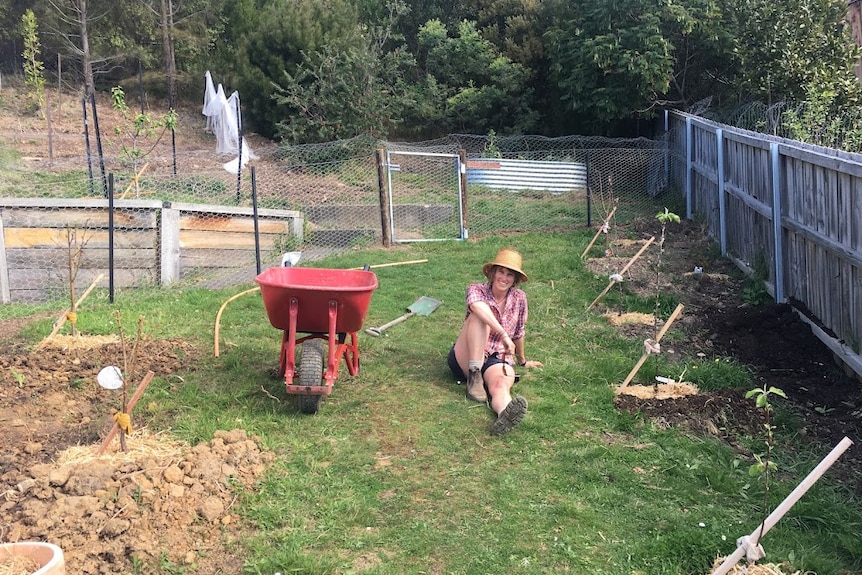 Woman sits in her garden, relaxing after planting fruit trees in clay soil in Hobart, Tasmania.