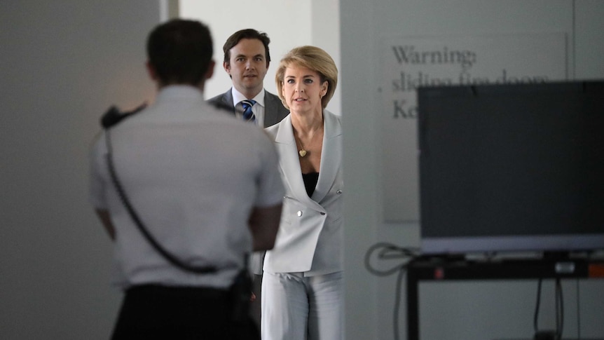 Senator Michaelia Cash is shielded from the media by a whiteboard, while wearing a white suit.