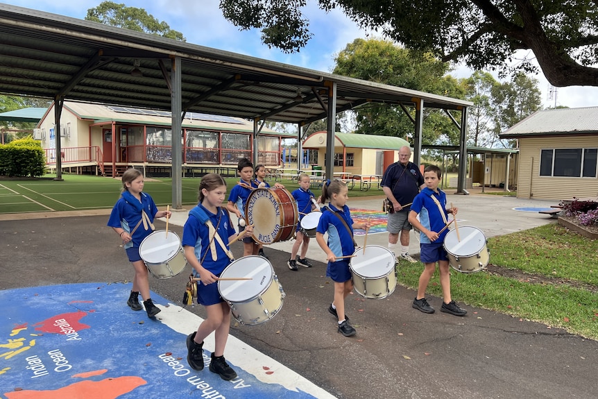 Group of children in blue school uniforms walks as they play the drums in a marching band