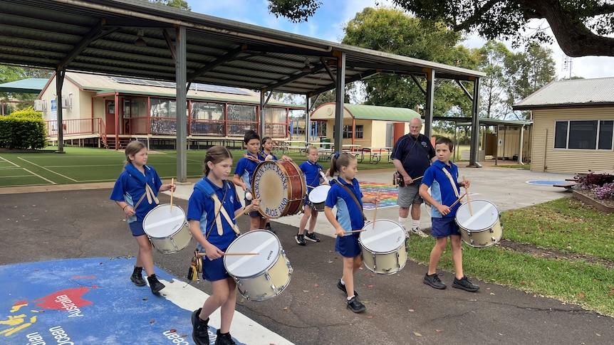 Group of children in blue school uniforms walks as they play the drums in a marching band