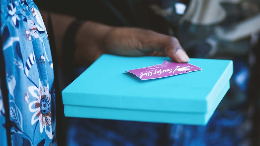 Woman holds a gift in a square box with a gift card sitting on top.
