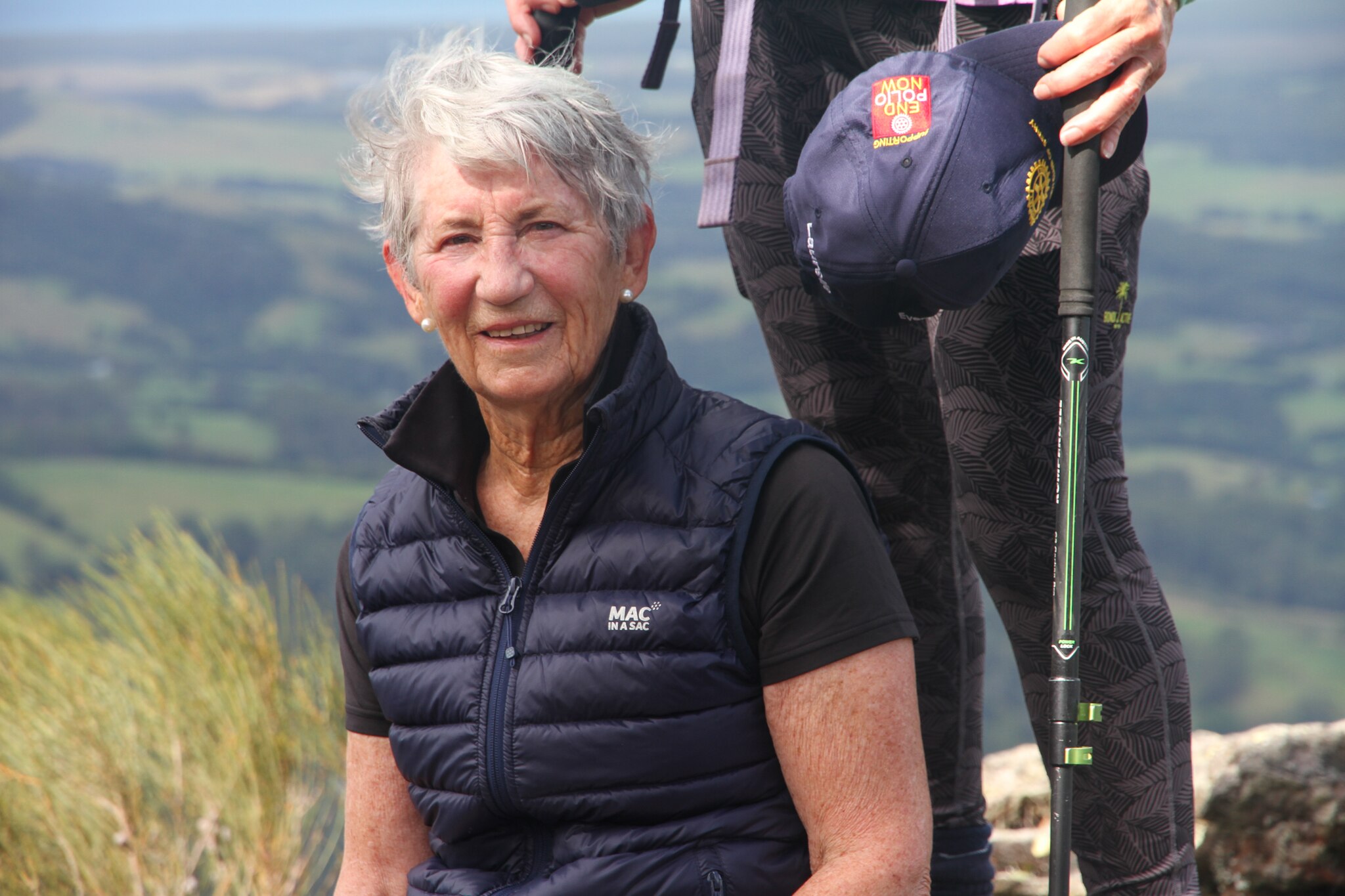 A woman smiles outdoors. She wears a puffer jacket.
