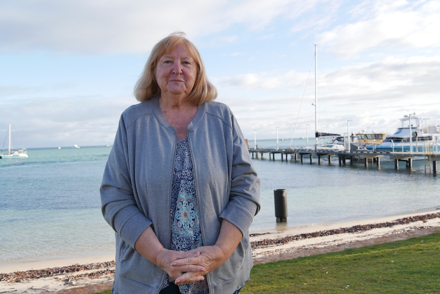 A portrait of a woman standing in front of the waterfront with boats and a jetty behind her. 