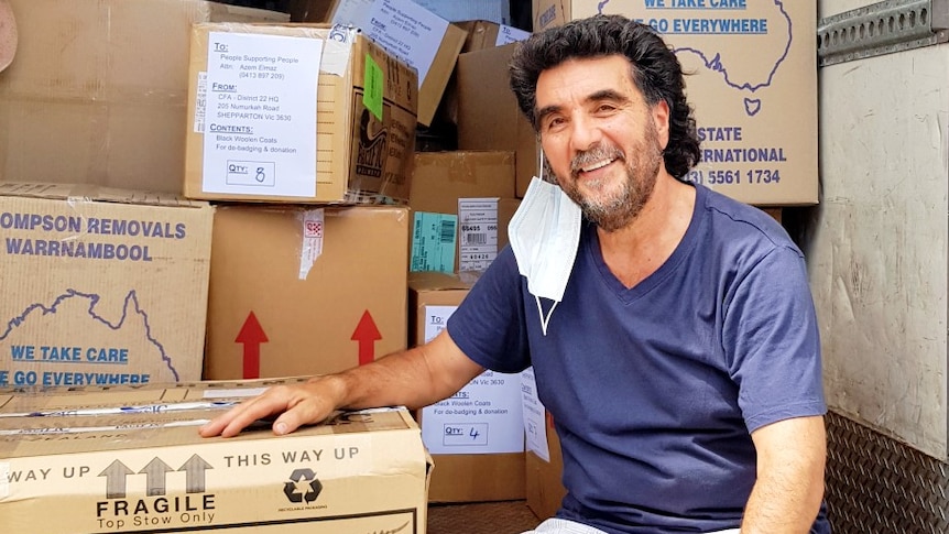 A man wearing sitting in the back of a truck filled with boxes.