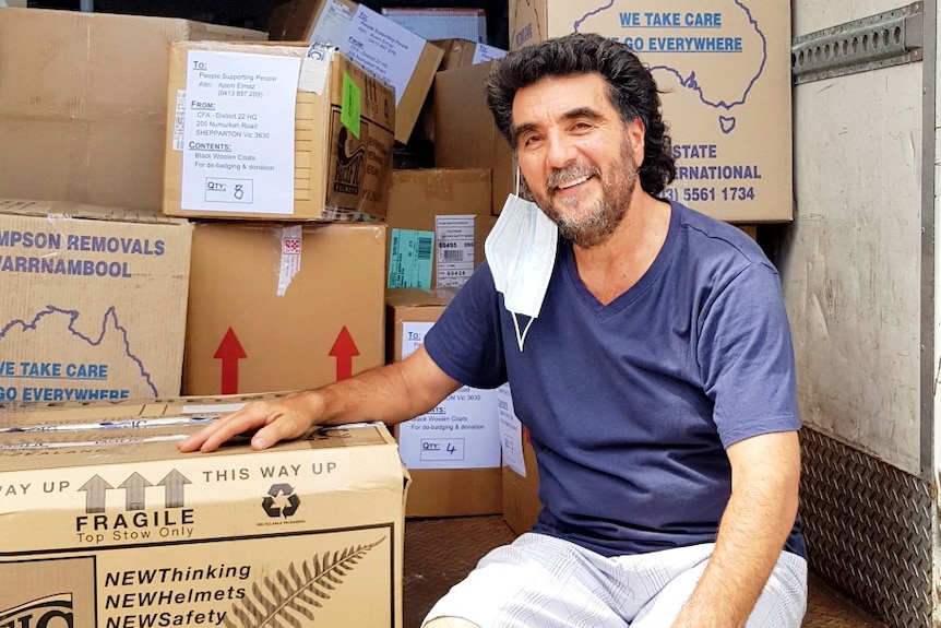 A man wearing sitting in the back of a truck filled with boxes.