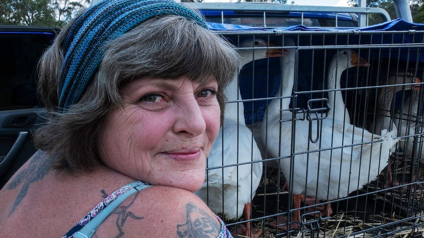 A woman smiles in front of a cage of geese