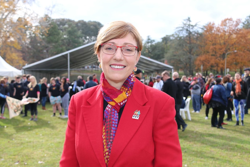 Rachel Stephen-Smith smiles, wearing an Indigenous scarf, a crowd of gatherers behind her.