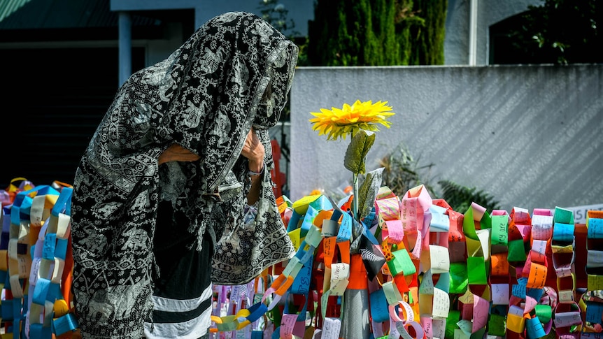 A mourner wears a black and grey elephant print shroud as they stand next to rainbow paper chains with messages on them.