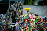 A mourner wears a black and grey elephant print shroud as they stand next to rainbow paper chains with messages on them.