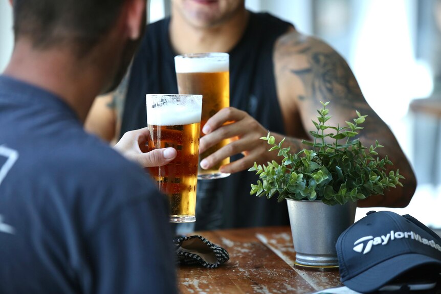 Two men clink their glasses of beer while seated at a table