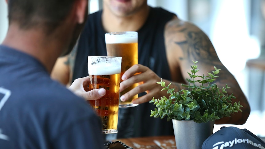 Two men clink their glasses of beer while seated at a table
