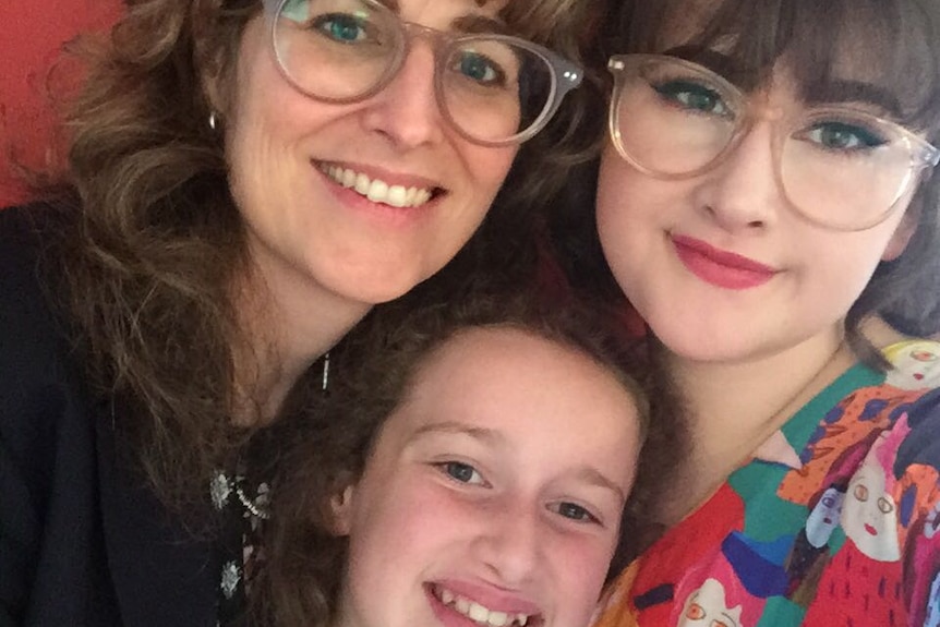 Woman with her teenage and tween daughters in front of a red background.