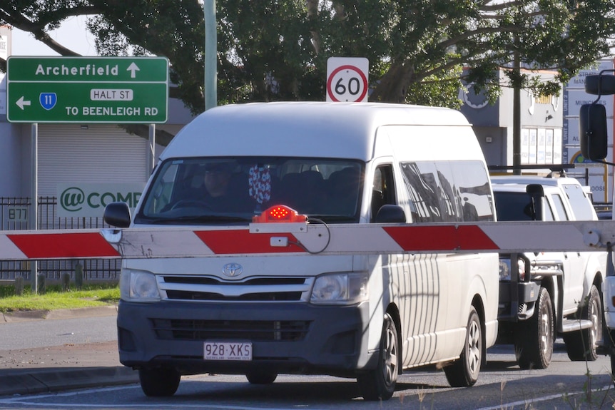 A van and other cars parked waiting behind a railway crossing.