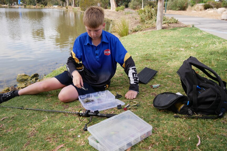 a young boy sits on the ground and picks a lure from his tackle box
