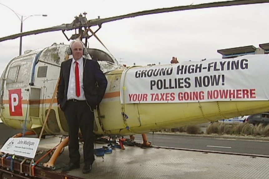 John Madigan standing in front of helicopter protesting politicians' entitlements