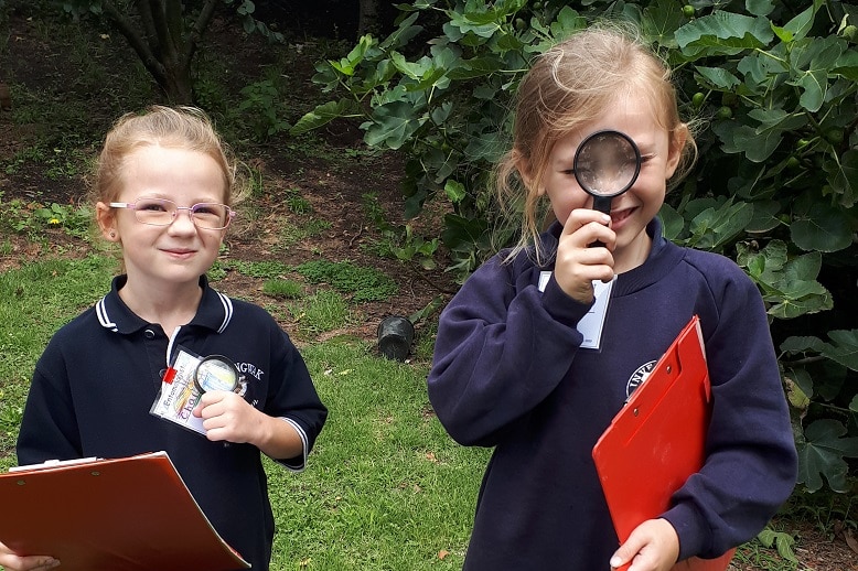 Two girl students with magnifying glasses and notepads