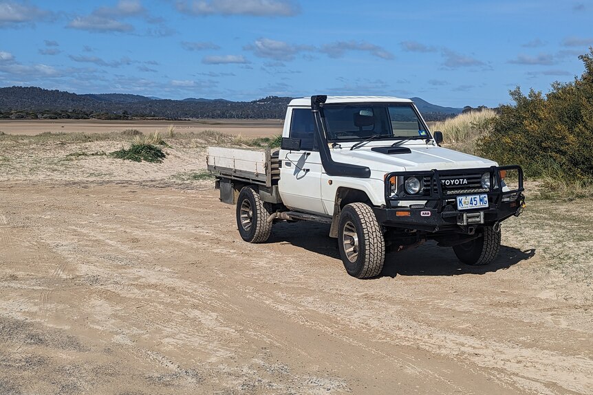 A white ute parked on sand near a river