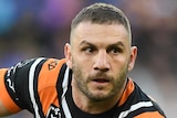 A male NRL player holds the ball in both hands as he looks to his left in preparation to pass the ball.