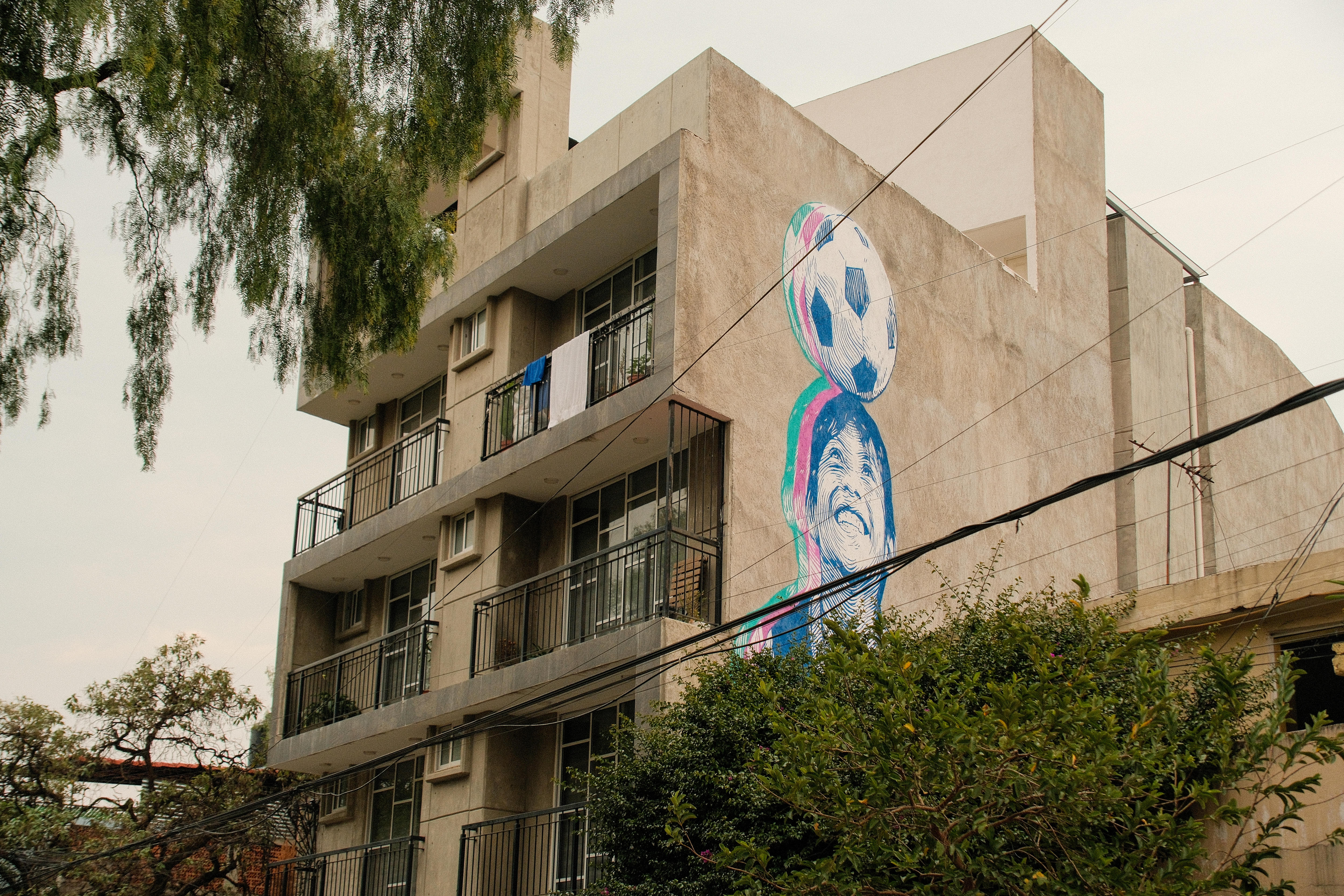 A mural of a boy headbutting a soccer ball on the side of an apartment building.