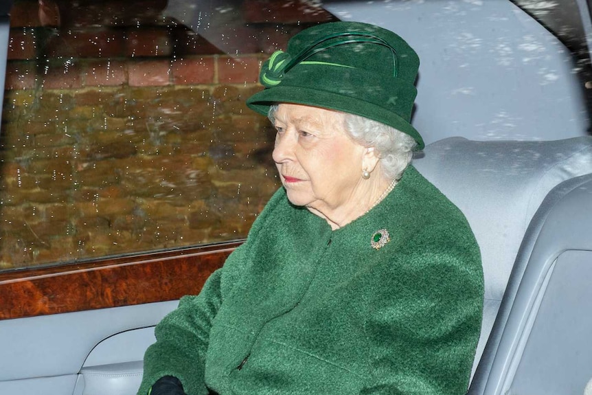The Queen sits in a car wearing a green coat and a matching hat.