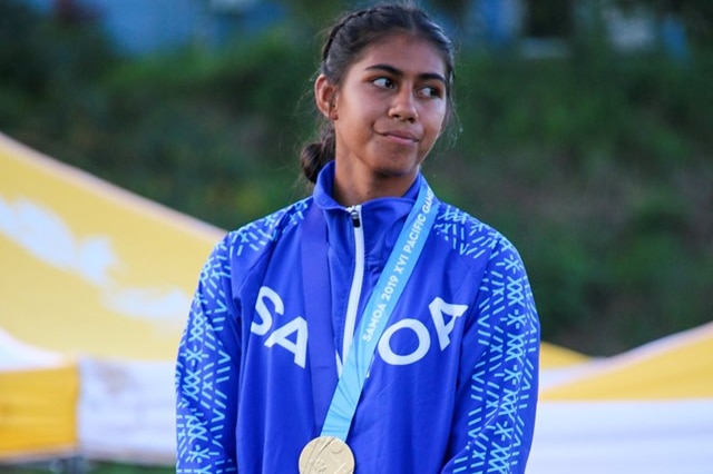 Jil Archer, wearing her national Samoa jacket, stands with a gold medal around her neck.