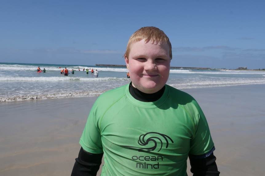 A boy dripping wet from the ocean smiles at camera with ocean in background