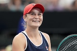 A woman wearing a red cap smiles holding a tennis racquet