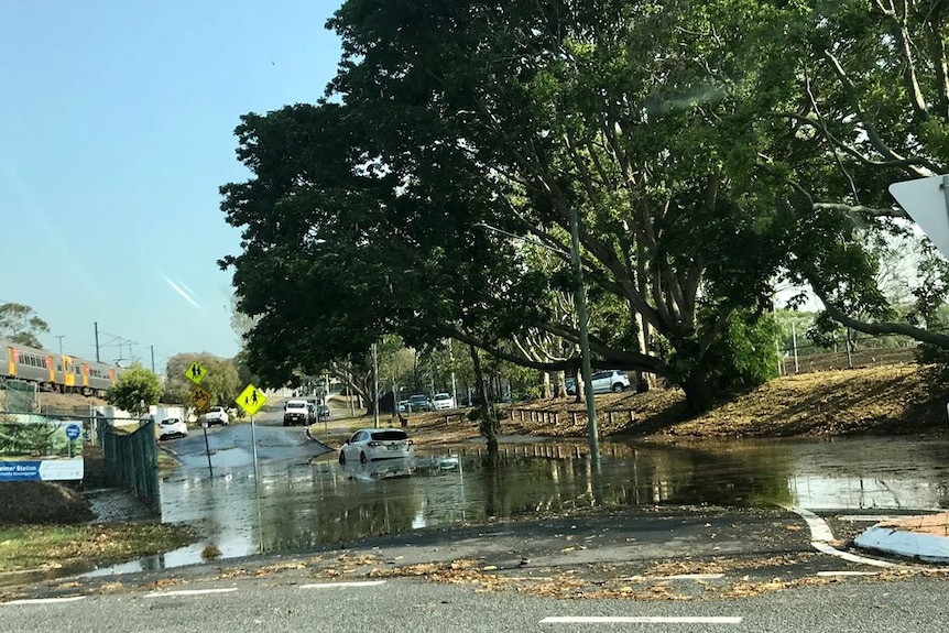 A white car drives through water next to a train station