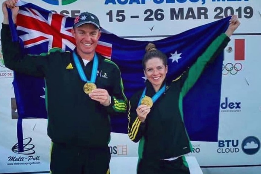 A man and a woman holding medals and a flag.