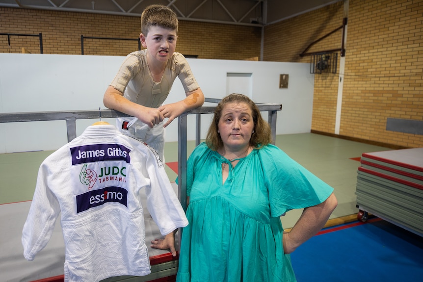 A young boy in a judo uniform standing next to his mother.