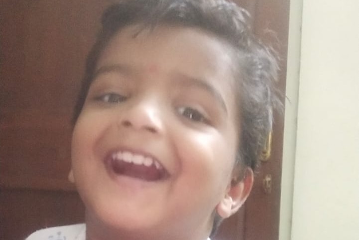 Young boy smiles at camera in white T-shirt.