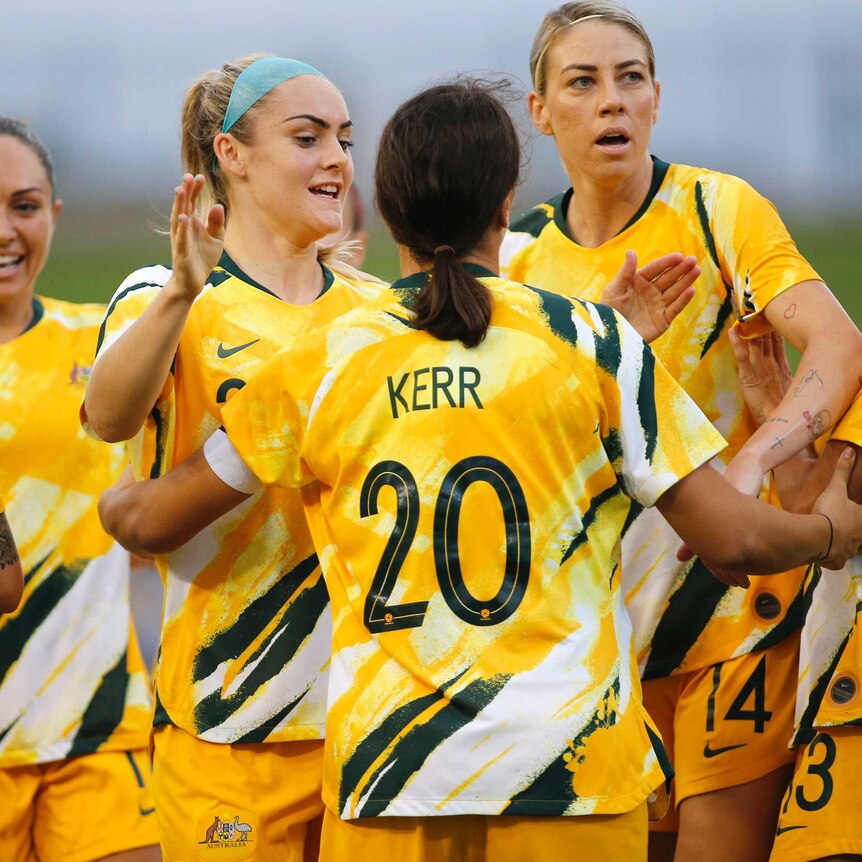 A footballer with her back to camera celebrates a goal with teammates in Olympic football qualifier.