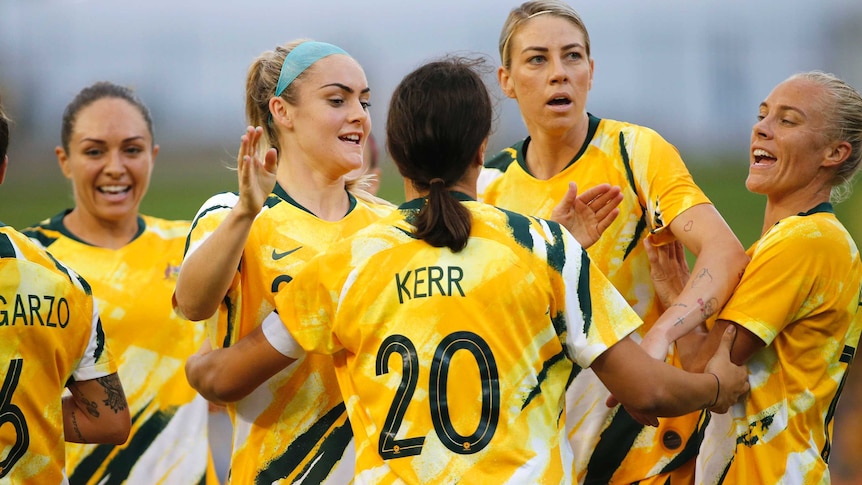 A footballer with her back to camera celebrates a goal with teammates in Olympic football qualifier.