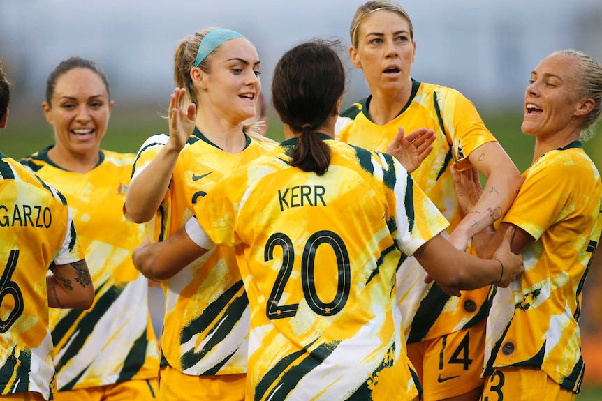 A footballer with her back to camera celebrates a goal with teammates in Olympic football qualifier.