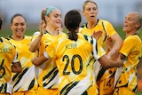 A footballer with her back to camera celebrates a goal with teammates in Olympic football qualifier.