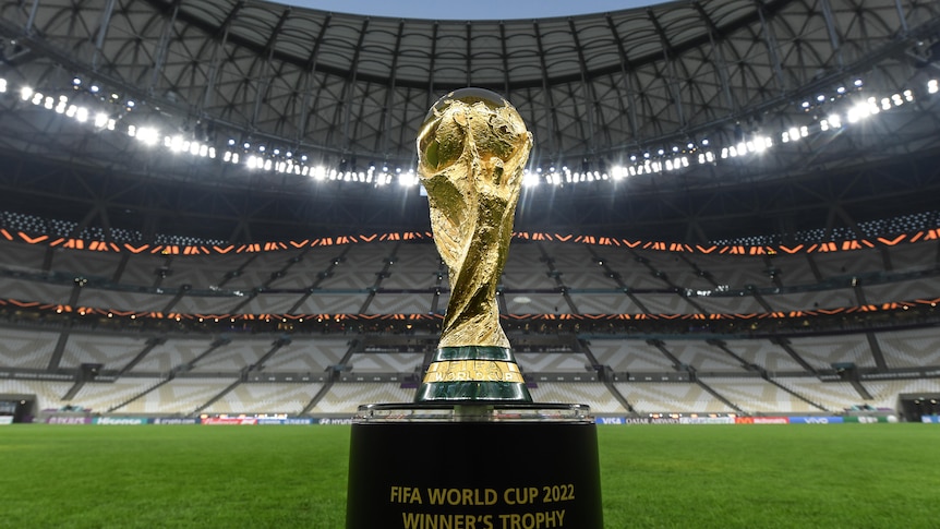 The FIFA World Cup trophy on a plinth in front of a stadium